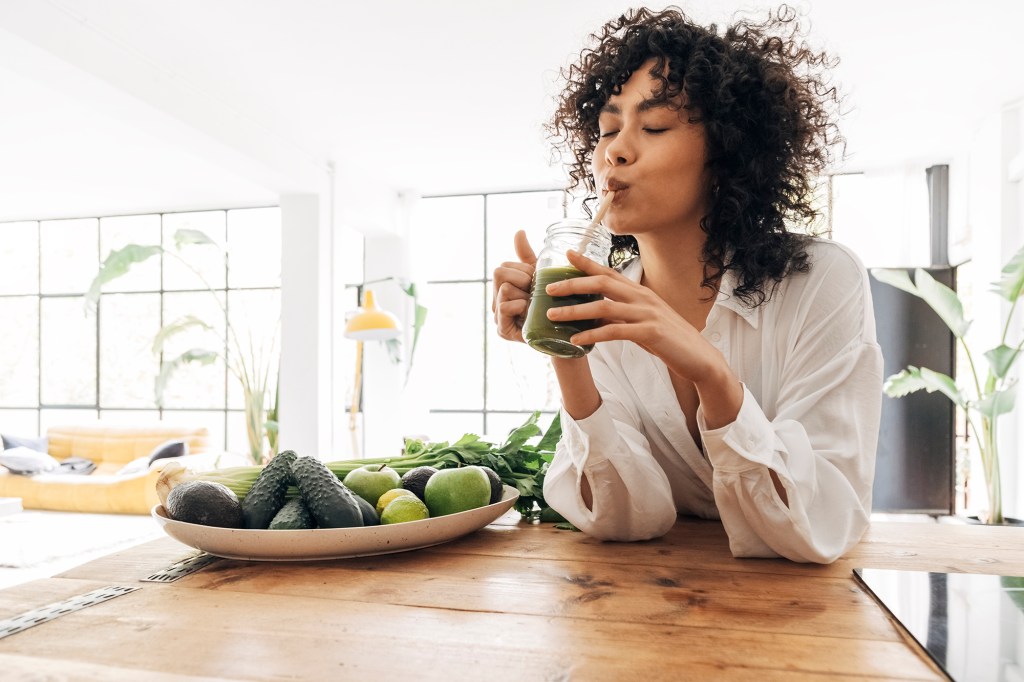 Young african american woman drinking green juice with reusable bamboo straw in loft apartment. 